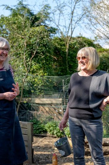 Smiling senior women enjoying gardening in a sunny backyard garden setting.